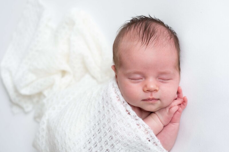 Baby in een ontspannen pose, gefotografeerd tegen een zachte bruine achtergrond. Newbornshoot thuis