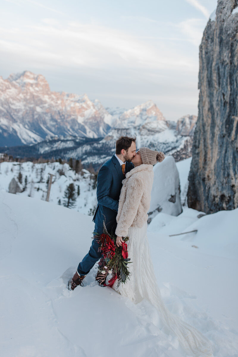 A couple. cradles each other's faces before a kiss. They are smiling with their eyes closed and the sun is shining goldem behind them.