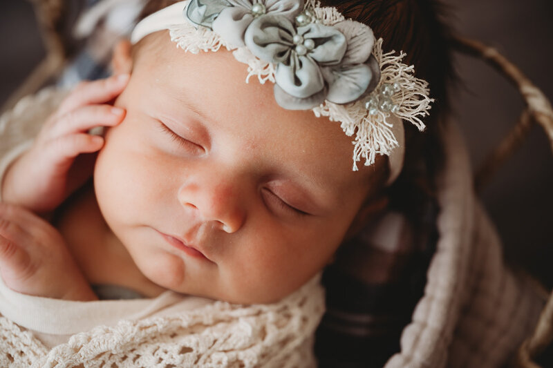 A tiny little newborn is snuggled up in a headband and outfit from the Nikii Pix Client Closet during her Bismarck studio session.