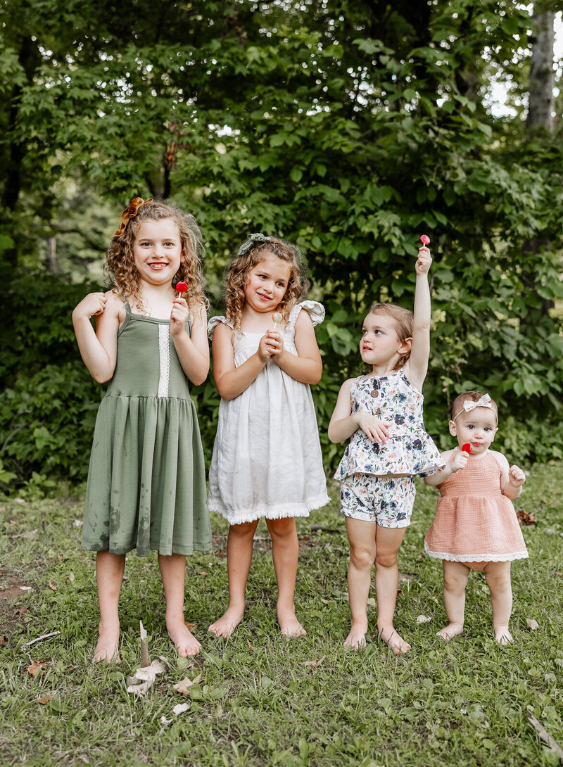 Four sisters standing in a row tallest to shortest eating lollipops during a lifestyle session by Jennifer Mosier Photography. 