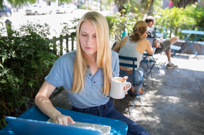 image of Krista Walsh sitting at outdoor table with coffee and laptop