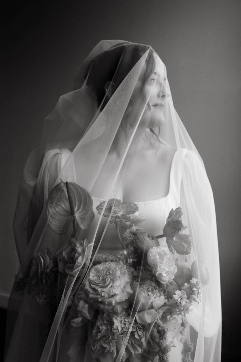 Timeless black and white bridal portrait under veil holding flowers, photographed in editorial fine-art style.
