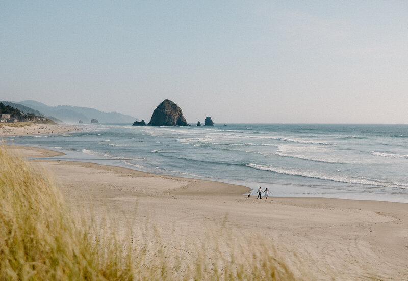 Wide shot of couple walking down Cannon Beach during their engagement session.