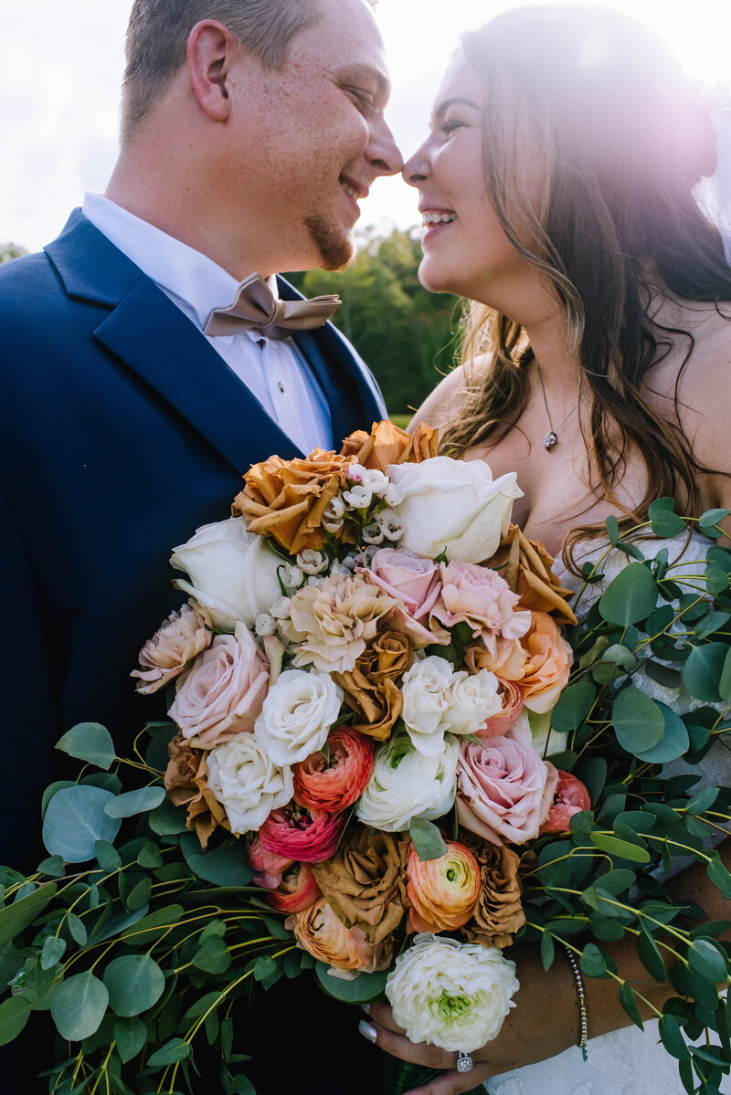 A happy couple nuzzles at Cedar Creek Ranch Weddings & Events as their wedding photographer looks on.