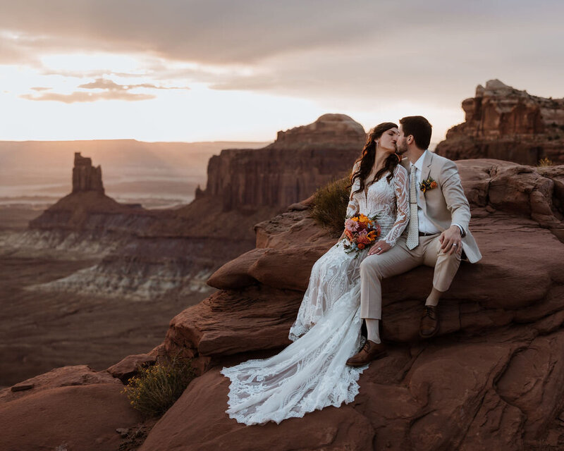 bride and groom sitting on a large red rock with the desert in the background