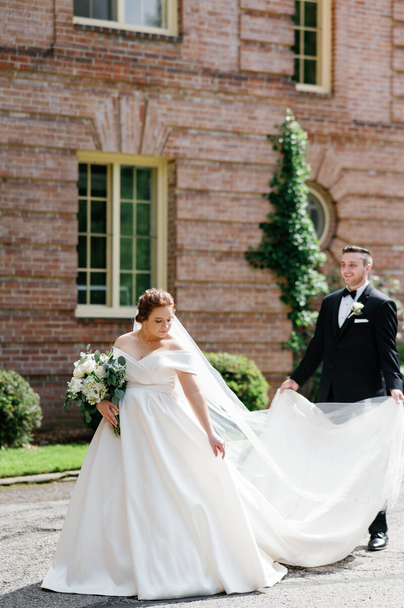 Bride and groom walking outside Kingwood Garden Center Manson | groom holding bride’s train | candid romantic Cleveland wedding photography