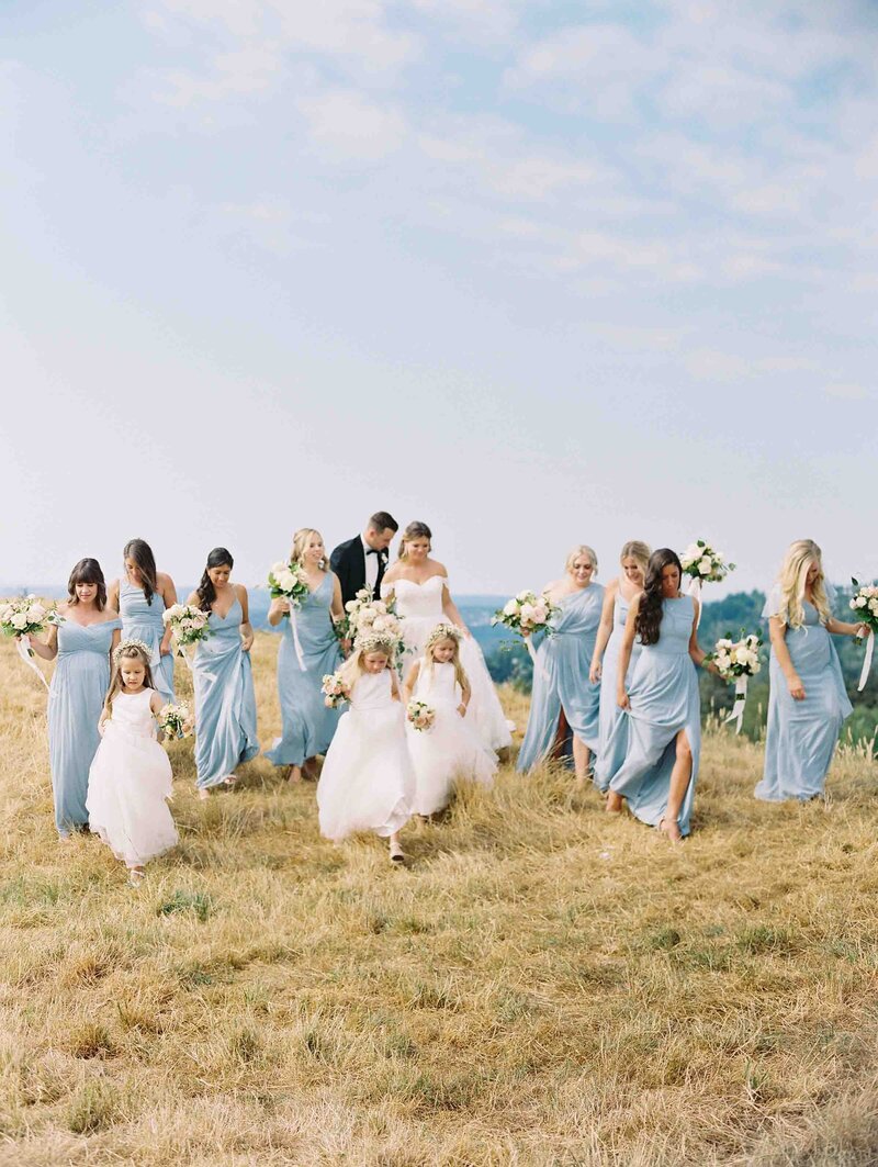 Seattle Wedding Photographers bridesmaids in light blue dresses walk with bride on golden grass hill