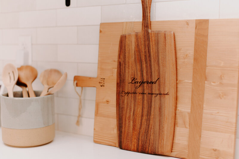 Two decor cutting boards and a container of wooden kitchen spoons in our kitchenette space.