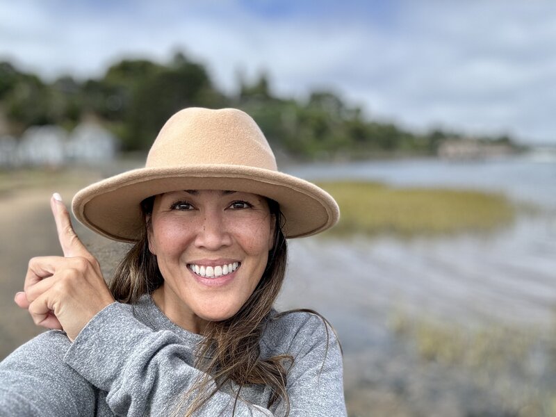 Woman on beach in  sweatshirt and tan hat