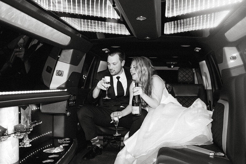 newlywed couple poses with champagne in limo after wedding