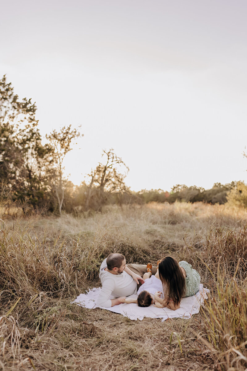 A dad looks off into the distance in a field while holding his son, who rests against his chest.
