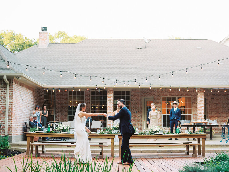 Landscape photo of bride and groom dancing under string lights