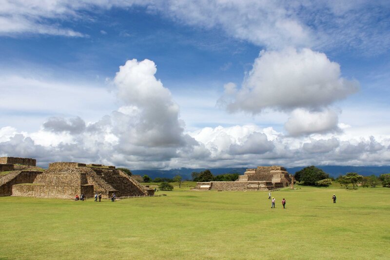 Ancient Zapotec ruins of Monte Albán in Oaxaca, with stepped pyramids and a vast green plaza under a sky filled with billowing clouds ©Stephanie Dosch | theViatrix Oaxaca Custom Travel Guide