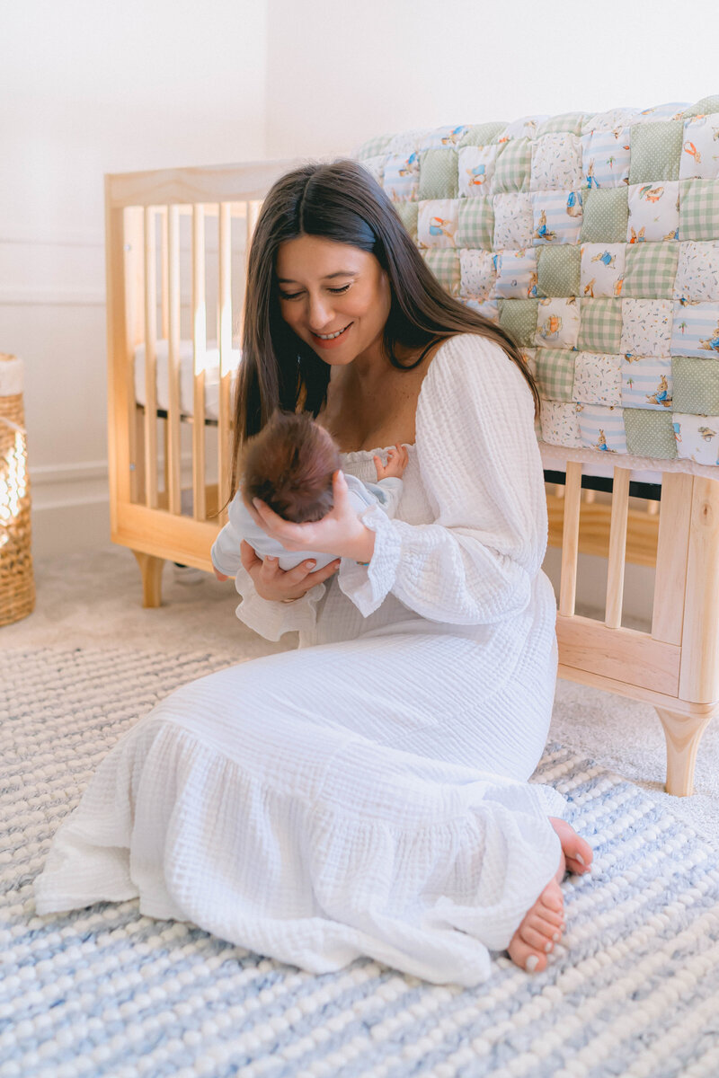 Newborn baby boy cuddled in mom’s arms near a sunlit window during an in-home newborn session in Salt Lake City, captured by a Salt Lake City newborn photographer.