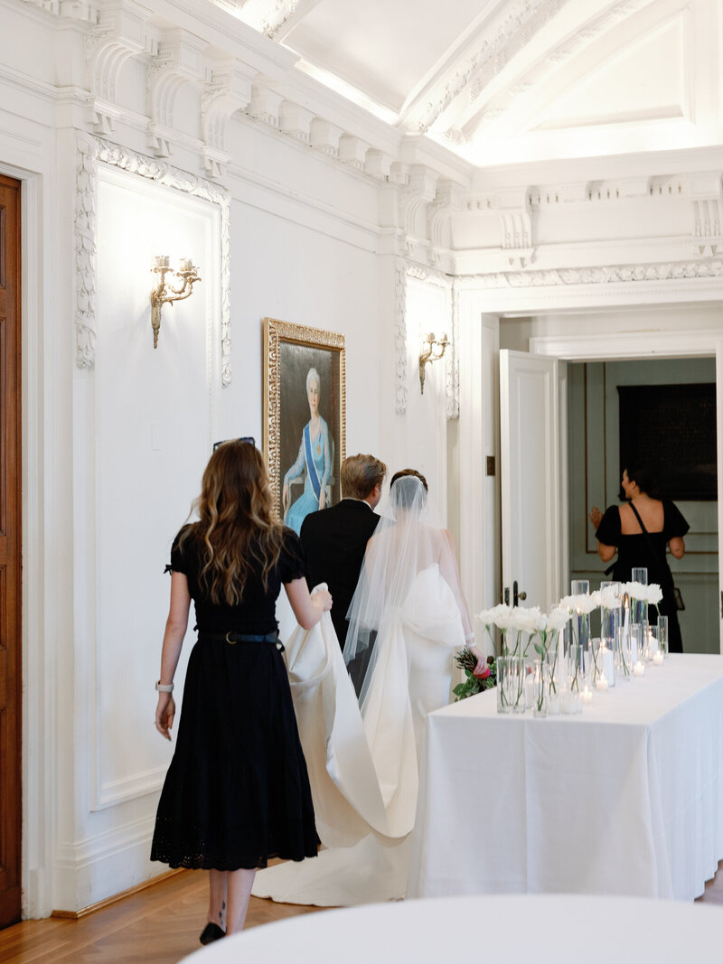 Wedding planner holds bride's dress as she walks through the reception hall at the DAR Constitution Hall
