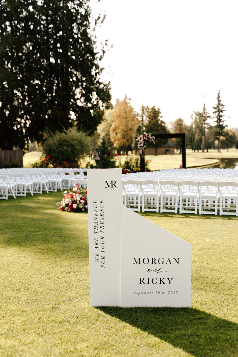 Wedding day-of-signage with chairs and flowers for a ceremony in the background, representing customized calligraphy offerings.