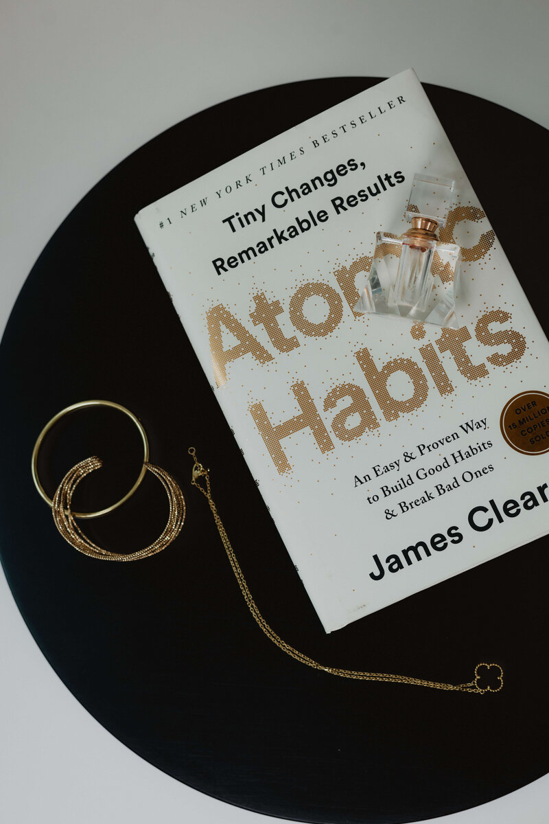 A black dish with gold jewelry and a book about Atomic Habits.