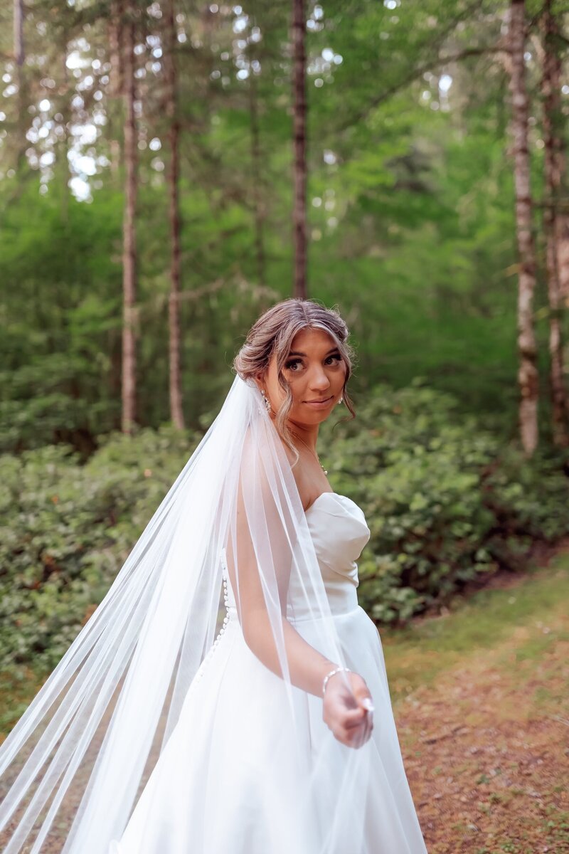 real bride wearing custom lace bridal veil while posing in forest