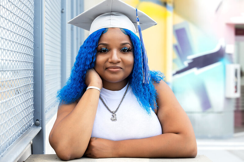 Senior girl wearing a white graduation cap posing casually on the rooftop at the Z Lot garage in Detroit, Michigan.