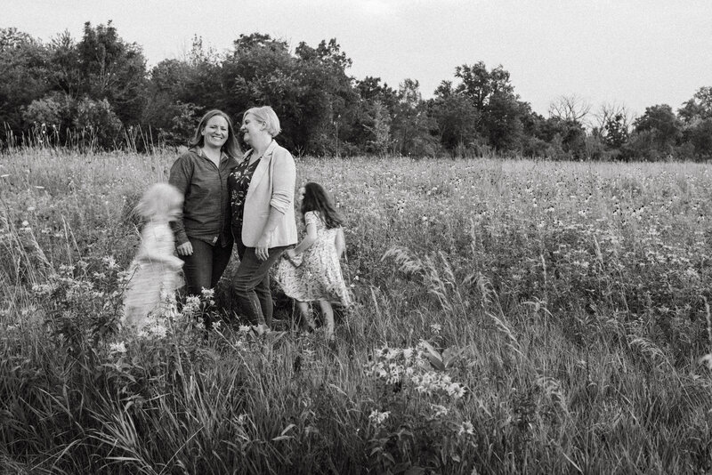 Two mothers with their daughters running around them in a field.