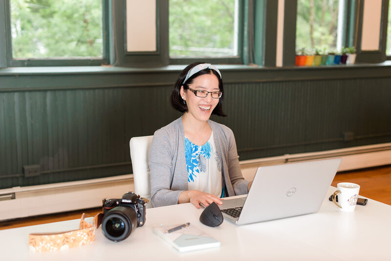 An Asian woman smiling and working on her laptop at a co-working space in Pennsylvania..