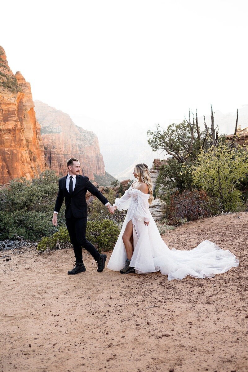 couple walking though a beautiful sandy area in zion with mountains behind.