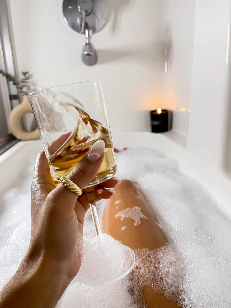 Woman holding up a wine glass wearing a ring and sitting in the bathtub