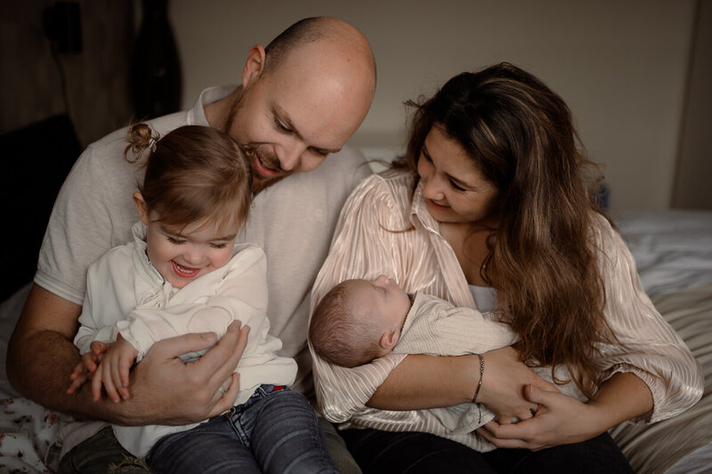 Ouders met hun dochter en newborn lachen met elkaar tijdens fotoshoot