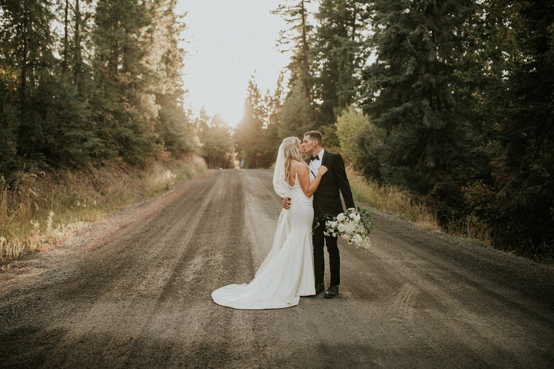 A bride and groom kiss one another on a dirt road