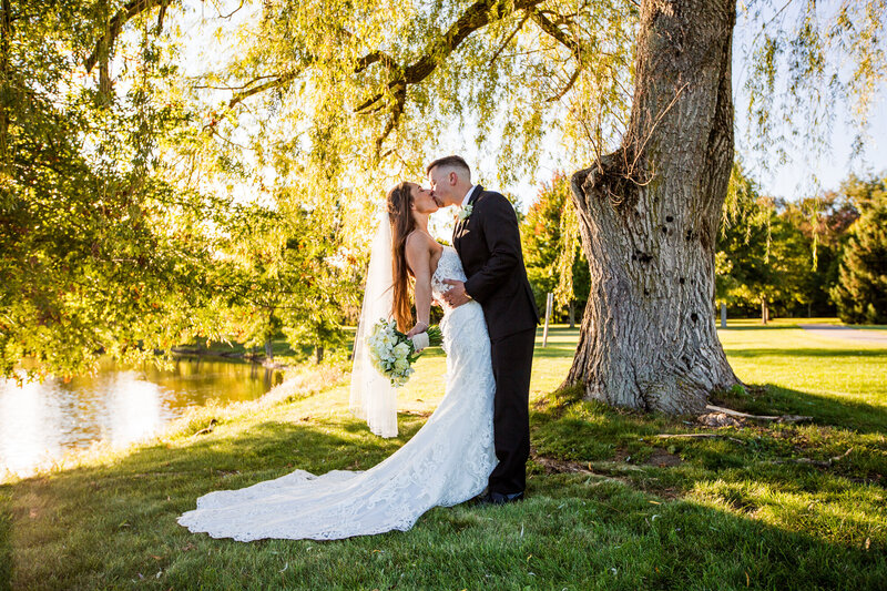 Bride and groom kissing under a willow tree on the Penn West Edinboro campus