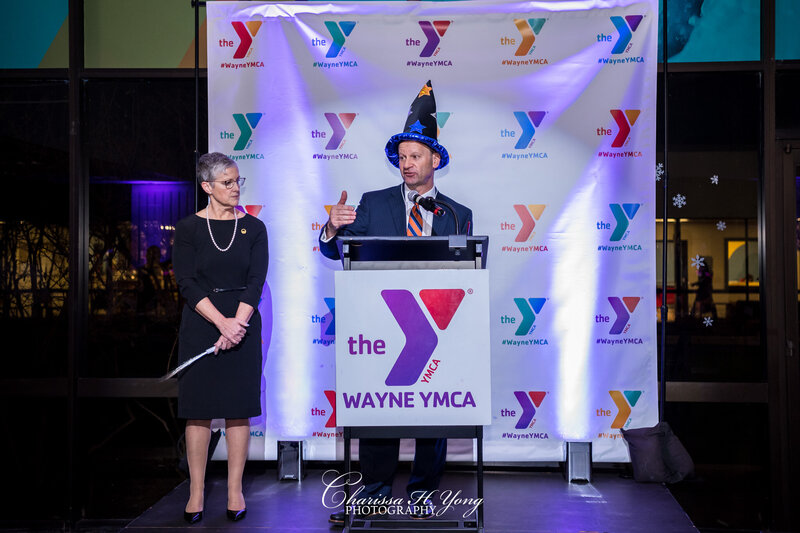 A man and a woman at a stage. The man is speaking to the audience at a YMCA fundraising gala.