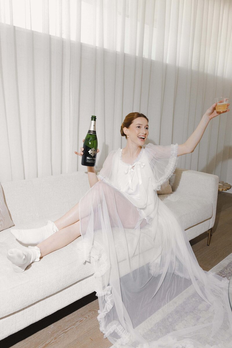 bride holding up cup and wine bottle on couch