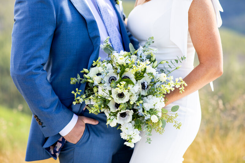 groom in blue suit and bride in her wedding dress hold bouquet of blue and white flowers