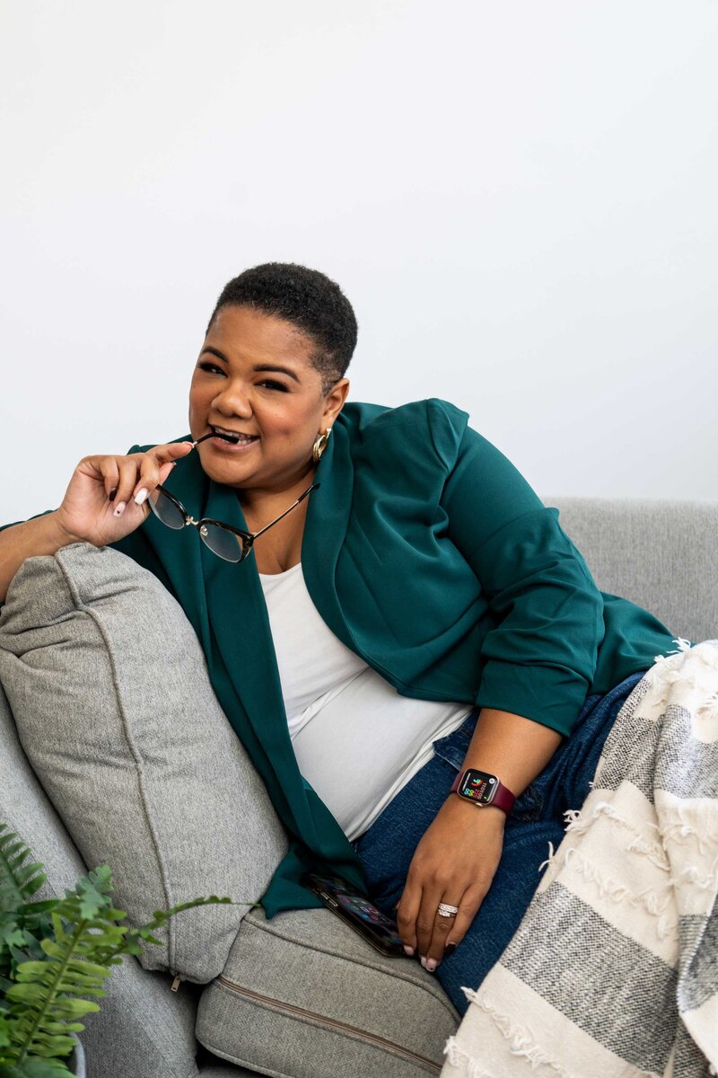 An expert in women’s career coaching sitting on a comfortable couch, wearing professional reading glasses and a green elegant branded outfit, symbolizing expertise and empowerment in career development for women.
