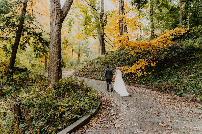 bride and groom walking on a winding path through fall trees