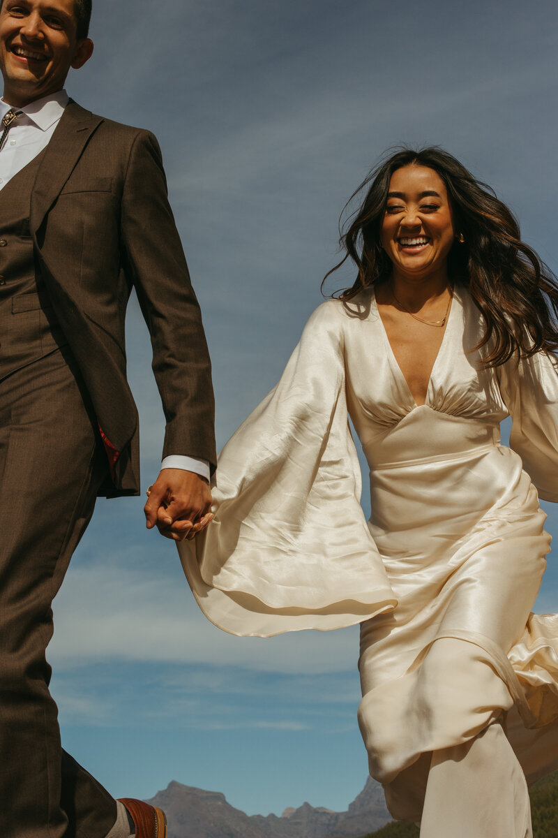 couple runs towards camera with mountains behind them