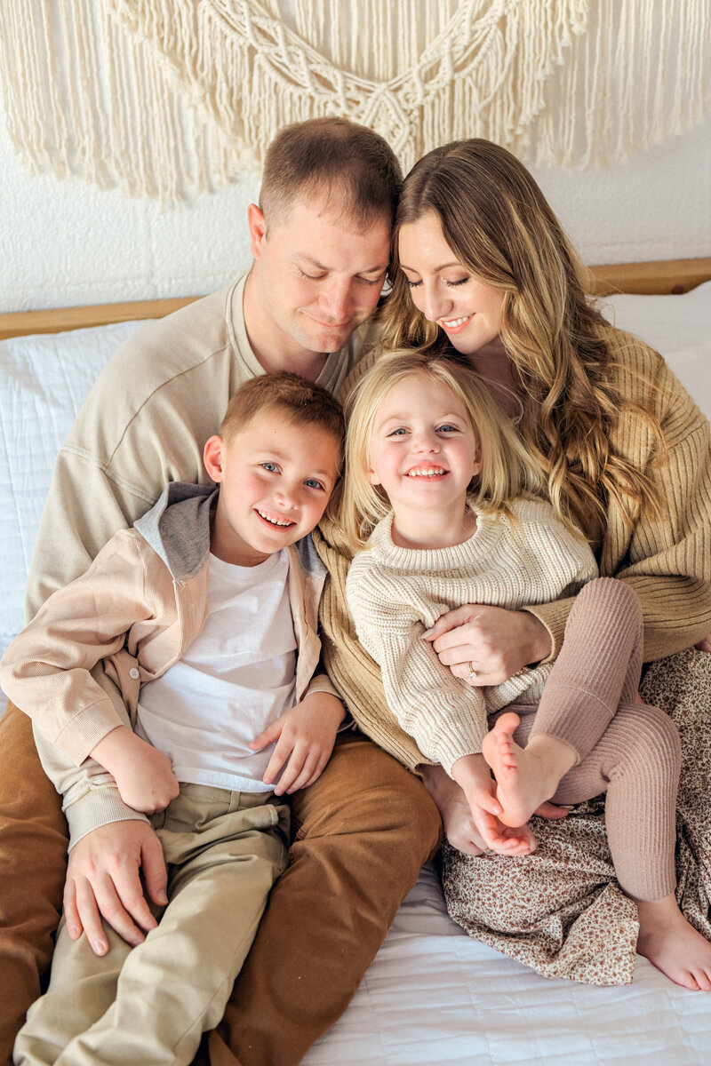 Family snuggle in bed for cozy family session in neutral colors.