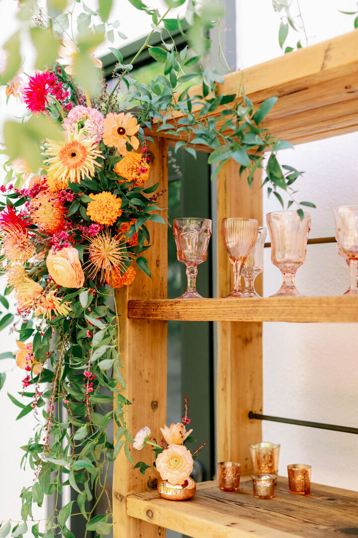 bouquet of bright flowers hanging on edge of wooden shelf with vintage wine glasses