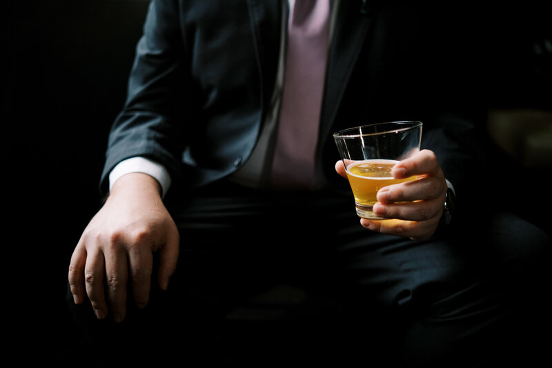 a groom sitting and resting a cocktail on his knee