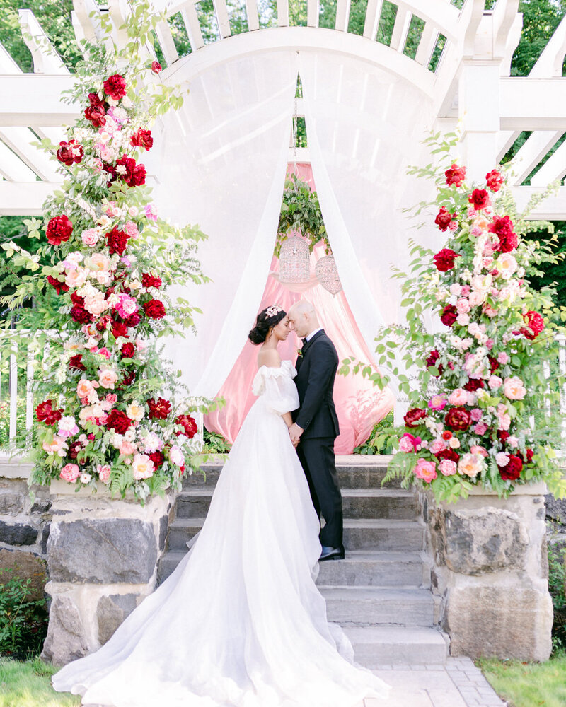A bride and groom embrace surrounded by pillars of flowers at their wedding ceremony at Stonehaven Manor.