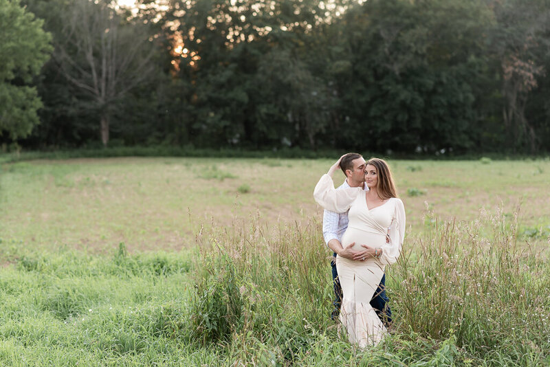 Couple in field, looking down at pregnant mom's belly