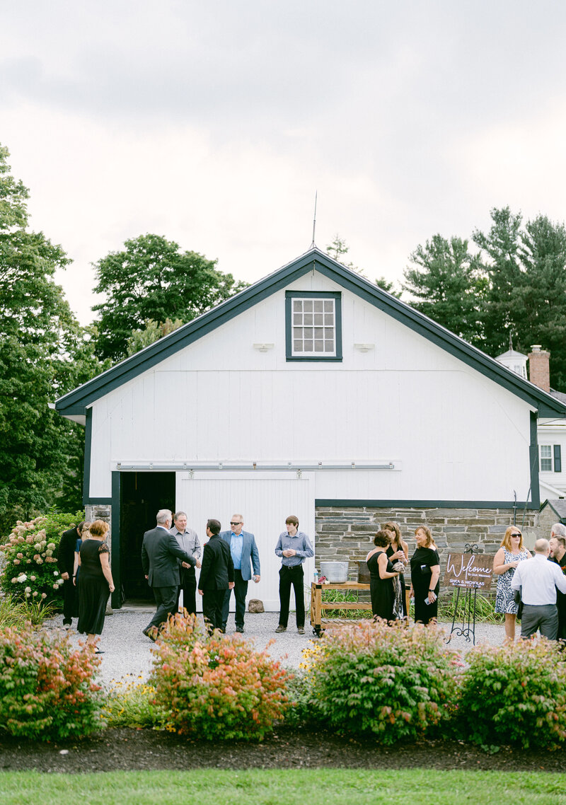 white barn with wedding guests mingling at outdoor wedding venue in upstate new york