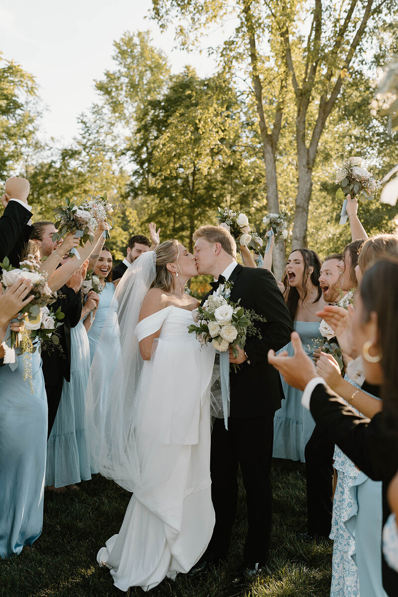 Bride and groom sharing a kiss surrounded by their cheering bridal party, celebrating their love and joy on their wedding day in Columbus, OH.