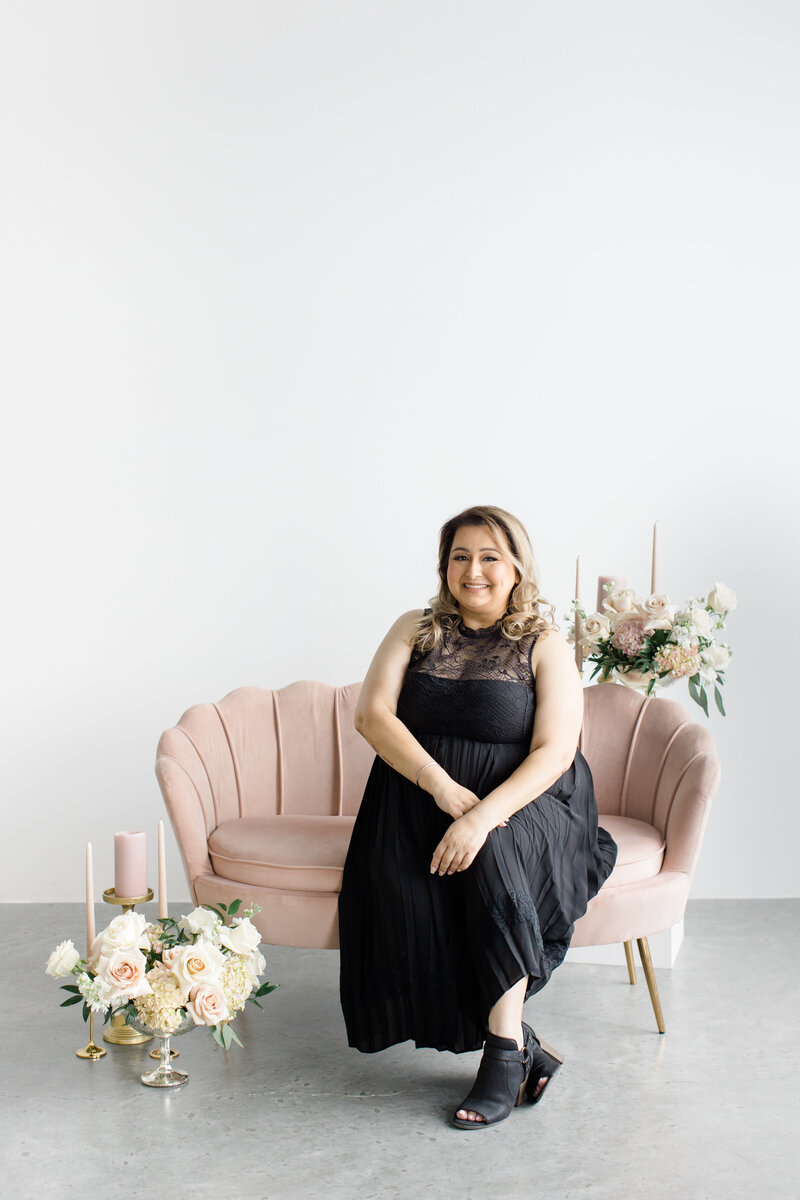 wedding planner sitting at a small white table next to a white teapit and a floral filled pink telephone booth