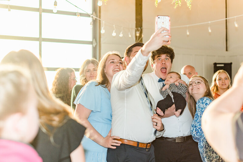One the dance floor living the dream holding a baby and having a live action "But first, let me take a selfie." moment.