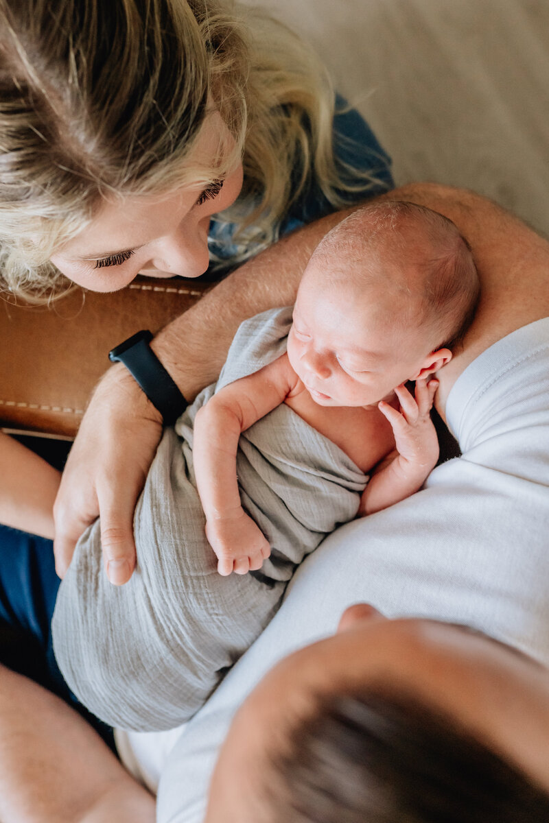 A close-up shot of a newborn baby swaddled in a soft blanket, nestled in the arms of a parent.