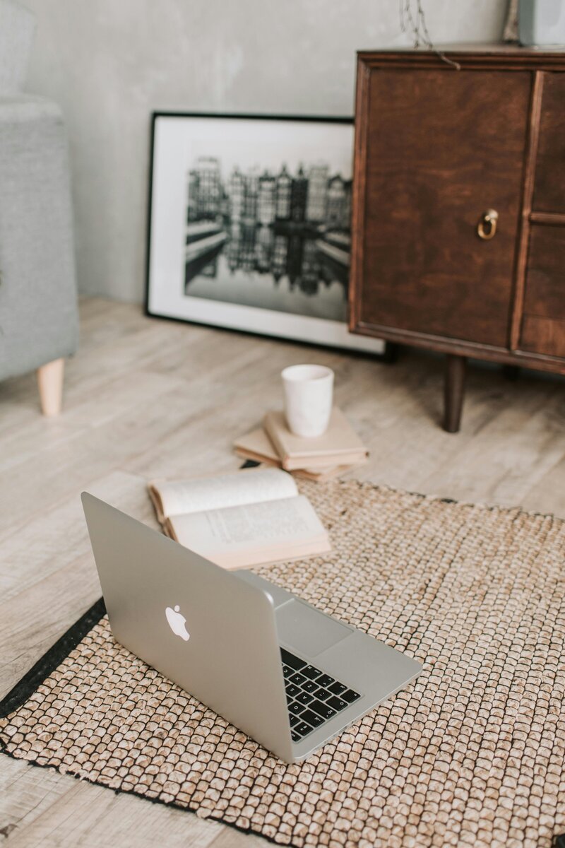 Macbook Pro laptop on the rug on the floor next to books and a couch