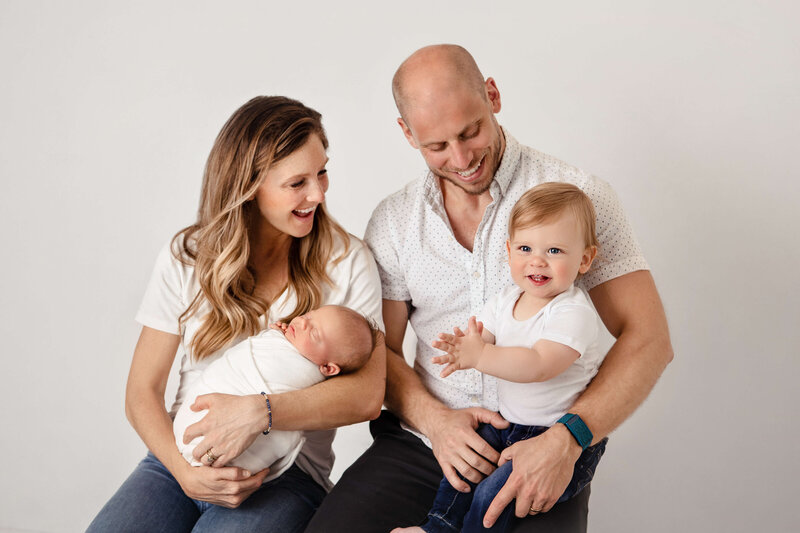 young family and their newborn baby and toddler son in white shirts and jeans