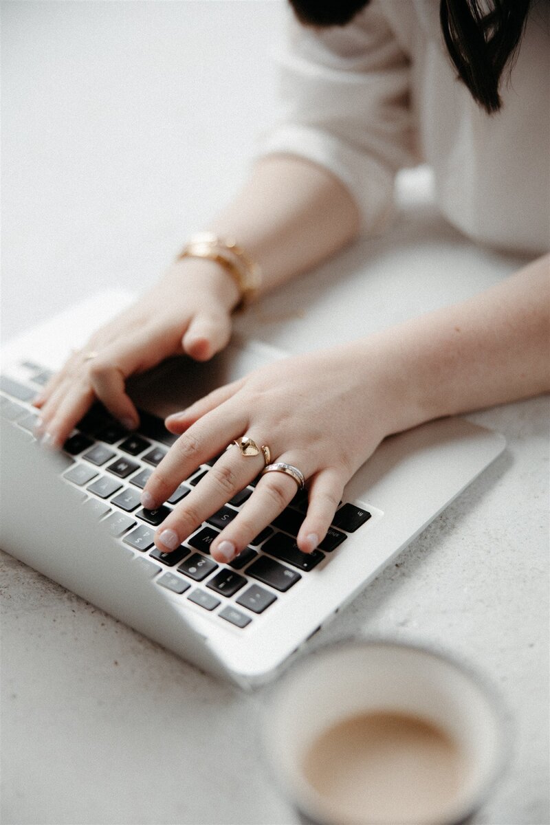 Close-up of hands typing on a laptop keyboard with a coffee cup in the foreground, symbolizing KP Virtual Assistance's hands-on approach to providing ongoing administrative support tailored for photographers