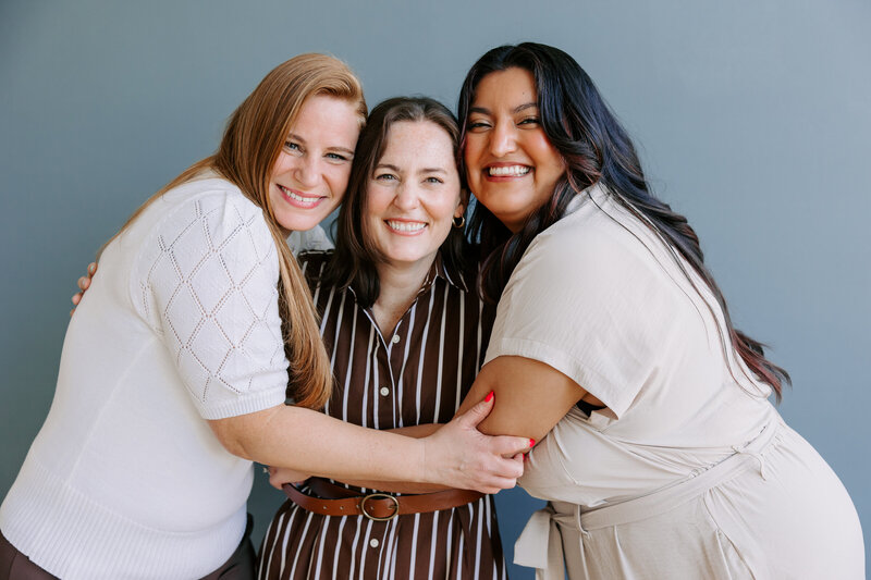 The Bridget Mary Team: Alicia, Bridget, and Vanessa embrace one another closely while smiling at the camera.